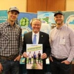 3 men standing in front of poster