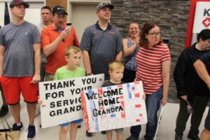 Honor Flight veteran is welcomed at airport by grandchildren with signs.