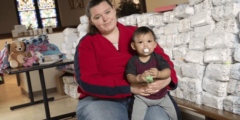 Mother holds baby next to a pile of diapers