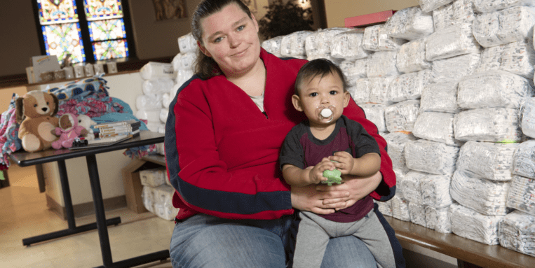 Mother holds baby next to a pile of diapers