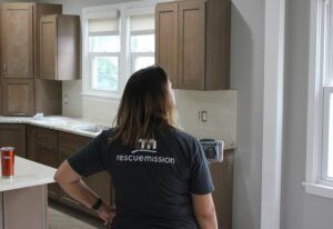 Tori Shires, in a Rescue Mission shirt, with her back to the camera looks at the renovated kitchen