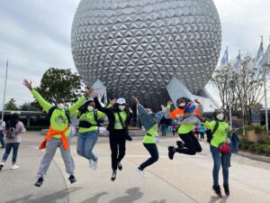 Kids in bright green shirts jump in the air in front of Epcot Center.