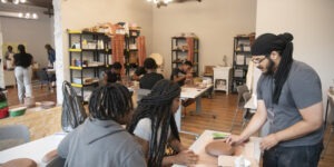 Person standing at table, with two people sitting at table with clay art